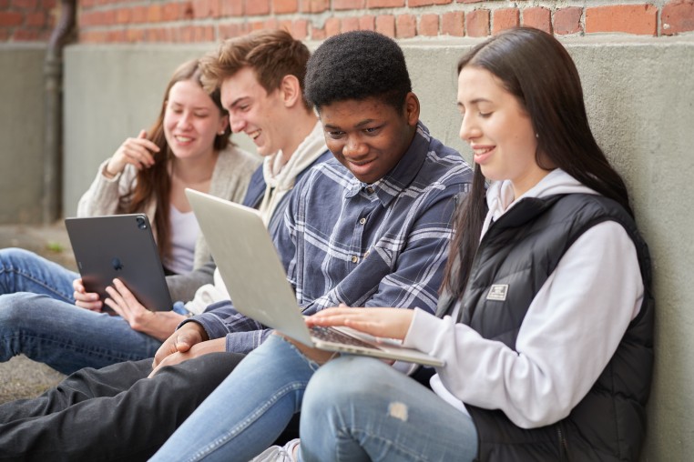Schüler*innen mit Laptops an einer Mauer sitzend.